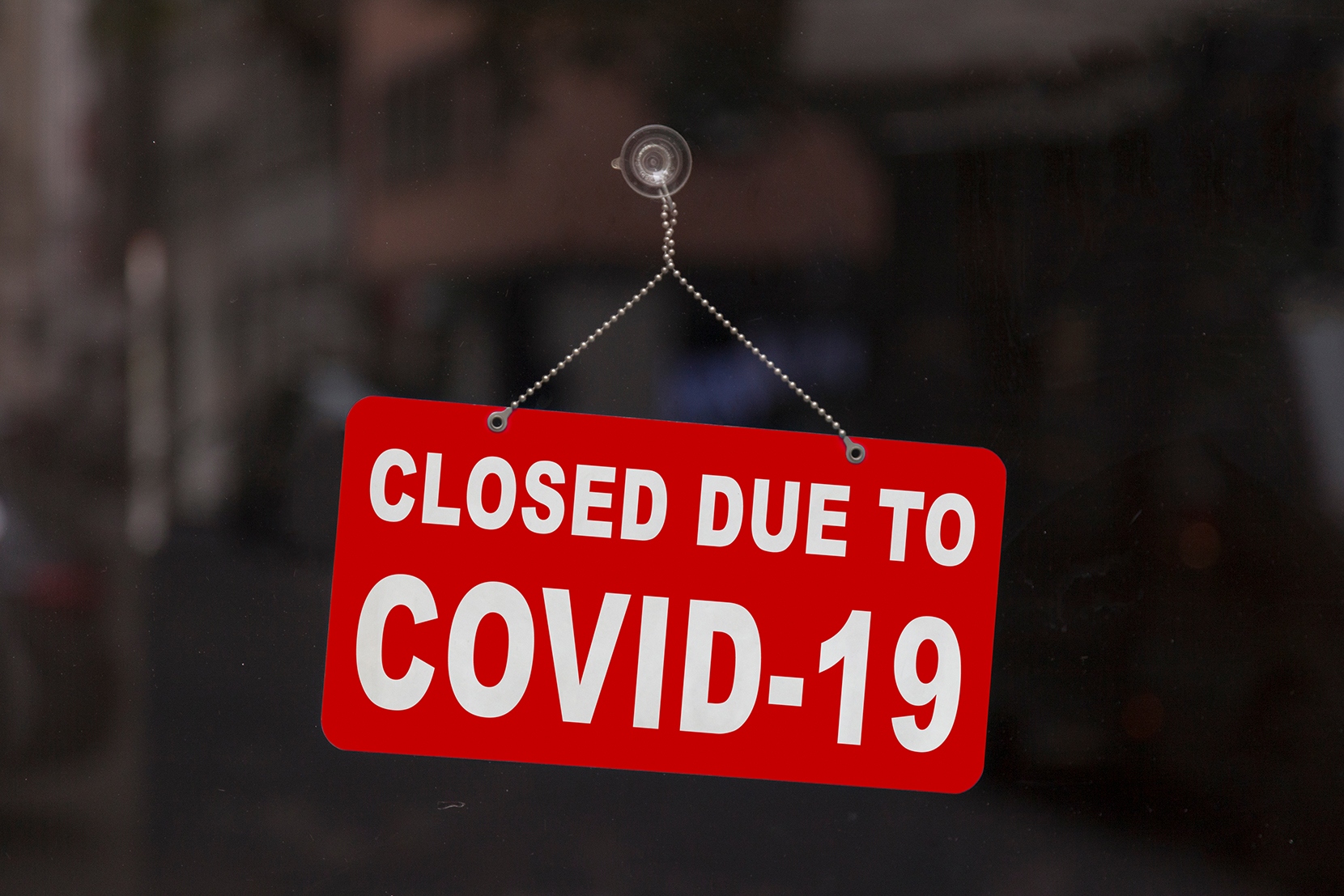 Red and white closed due to COVID-19 sign hanging in a window.