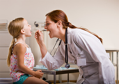 Female doctor asking a little girl to say “Ahh,” to look in her throat.