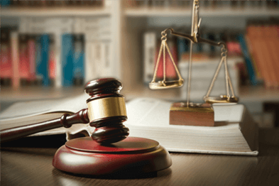 Close-up of a judge’s gavel and scales on a table in a library with books in the background.